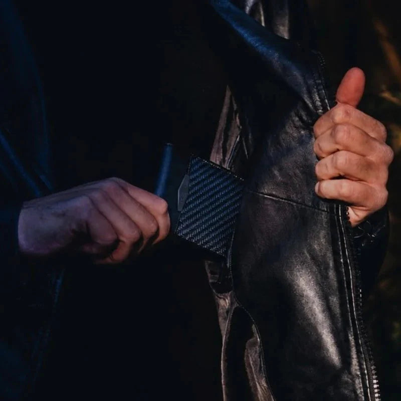 Man in leather jacket pulling a carbon fiber COLDFIRE wallet from inner pocket against urban night skyline
